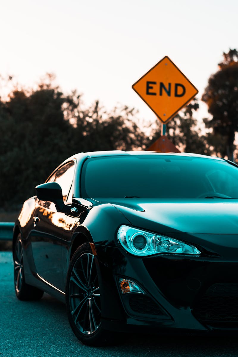 Stylish black luxury auto parked near a road end sign, surrounded by lush greenery.