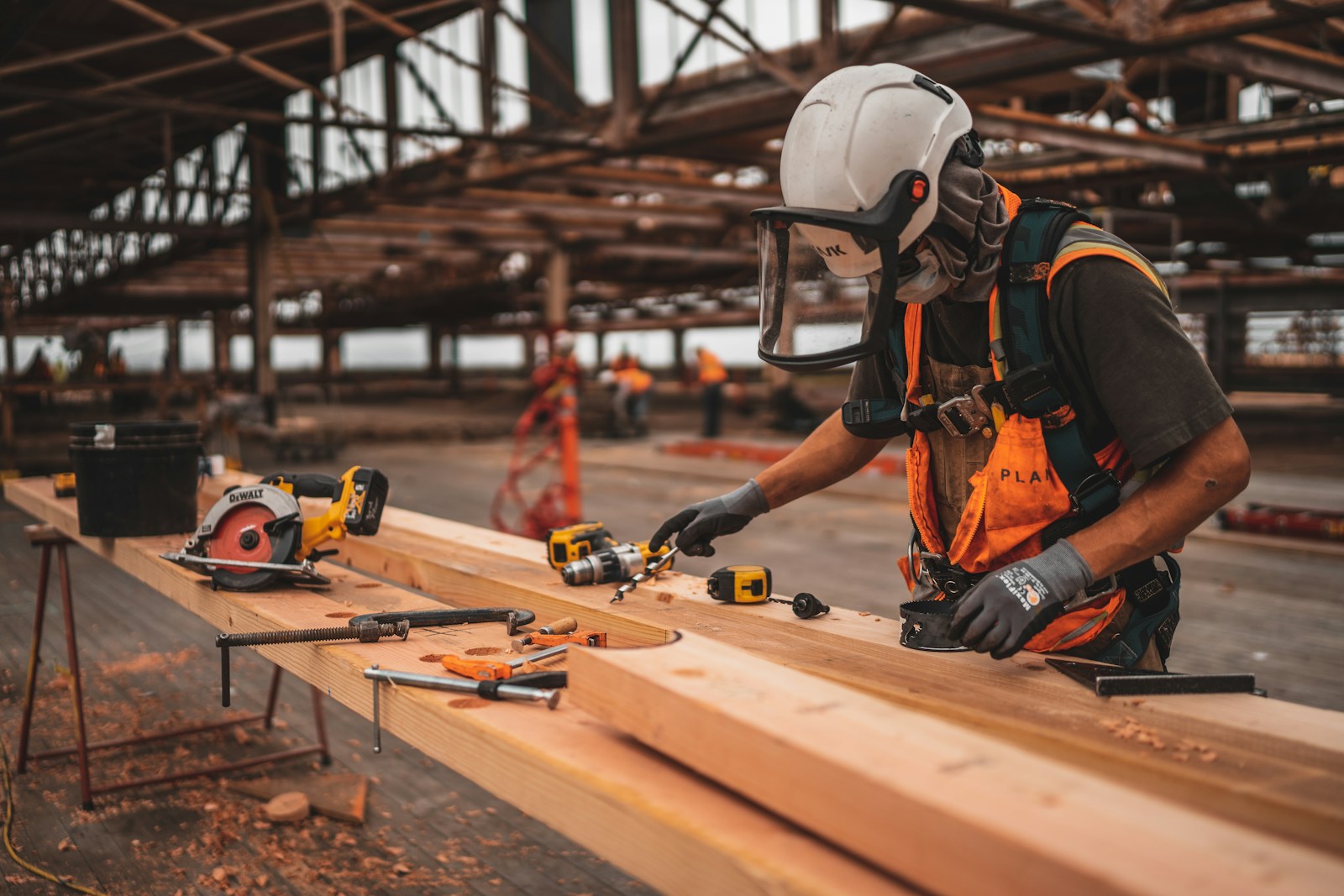 Builders, man in orange and black vest wearing white helmet holding yellow and black power tool